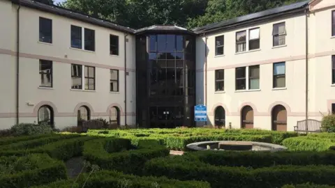 Guy Henderson/ LDRS A three-storey council building with a glass tower in the centre and a green knot garden in the foreground.