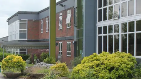 Chiltern Hills Academy, showing a school with red brick, a large number of windows, and a number of bushes and plants. 