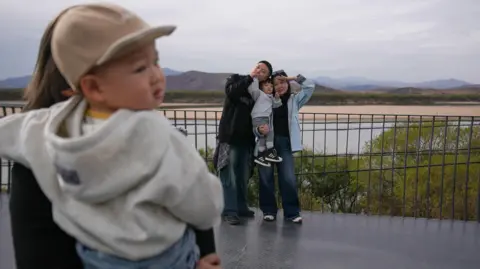 BBC A couple with a toddler poses for photos on the building, with a view of North Korea behind them 