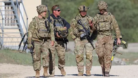 US troops walking during a training exercise in Germany. They carry rifles and wear camo