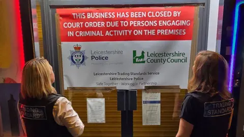 Leicestershire County Council The exterior of Roman Express with a closure sign across the front door and trading standards officers looking at it