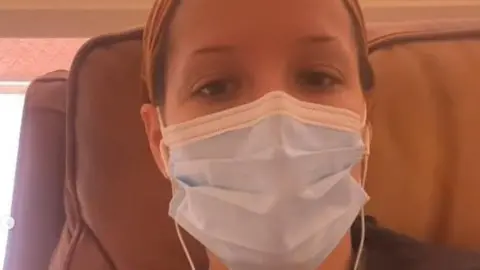 INSTAGRAM/@iamhalsey Halsey, wearing a medical mask, pictured in an arm chair on her first day of treatment. She has brown eyes and wears her hair up in an orange bandana.