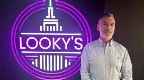 Smiling man standing in front of an illuminated sign with the name Looky's on it