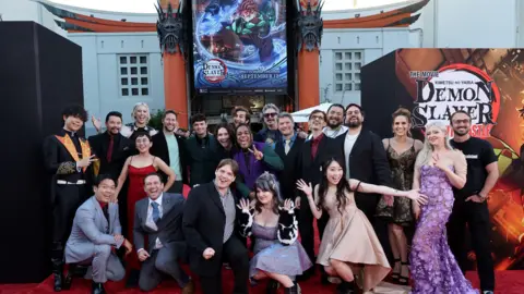 Un grupo de personas que usan imágenes y vestidos de muelle se acumula fuera de una película en la alfombra roja, Slayer Demone, carteles para Kimets No Yaiba Infinity Castle. Ceremonia de estado mental.