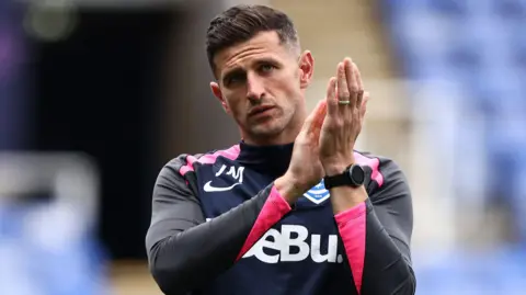 John Mousinho applauds the fans after a game.