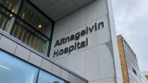 Image with sign saying Altnagelvin Hospital against grey brick building