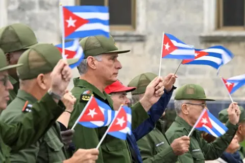 Cuba's President Miguel Diaz-Canel waves a Cuban flag alongwith others during a march outside the U.S. Embassy to protest against what they denounce as U.S. aggression in the region, following the capture of Venezuelan leader Nicolas Maduro and his wife, Cilia Flores, and the killing of Cuban soldiers in the U.S. strike, in Havana, Cuba, January 16, 2026. 