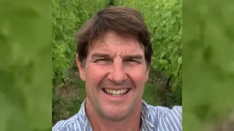 Kieron Atkinson A man with brown hair who has a resemblance to Tom Cruise stood in a vineyard. 