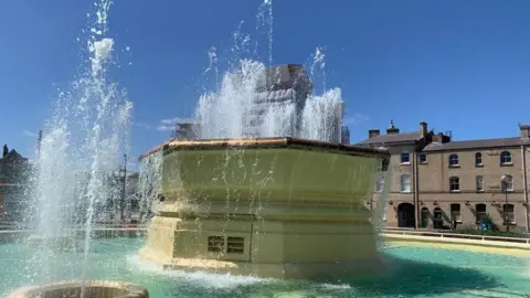 Hull City Council A large fountain, painted yellow, spurting out blue water under blue skies. 