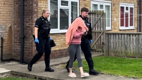 BBC A woman hidden under a jumper, escorted by police