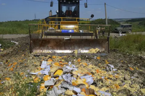 Reuters A bulldozer crushing a selection of cheeses