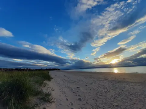 Tammy Travill A wide sandy beach at sunset in Nairn, with a dramatic sky dominating most of the frame.