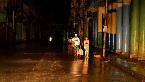 Reuters Three people walking down an empty road in complete darkness during the blackout