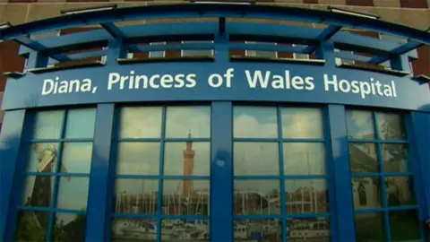 The main entrance to Diana, Princess of Wales Hospital in Grimsby. It is a blue curved, glass structure with images of local landmarks in the panes.