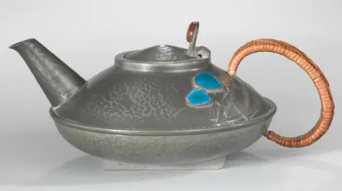 MNH A pewter teapot with a blue design and woven handle.