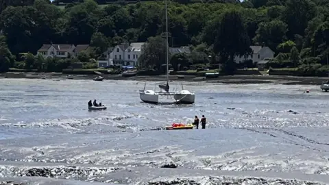 Falmouth Coastguard Rescue Team Coastguards working to rescue the people and dog in the dinghy stuck in the mud with a catamaran behind them