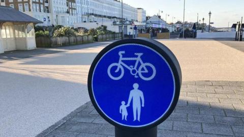 A cycling and pedestrian blue sign in front of the plaza