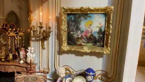 Olivia Richwald/BBC A miniature version of a painting with a gold frame on the interior wall of a dolls' house. 