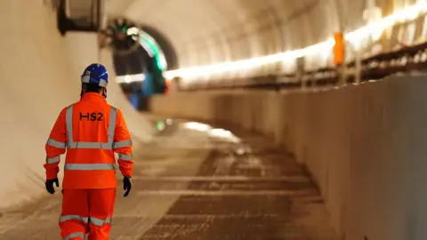 A man in hi-vis clothing, branded with the logo of HS2, walks through the Chilterns tunnel
