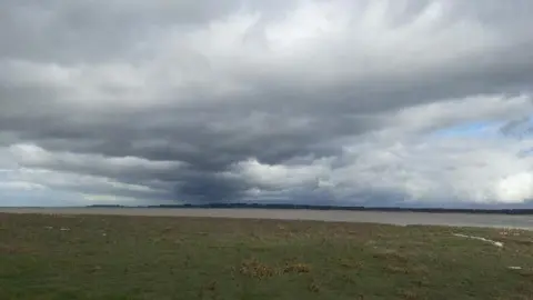 Dark clouds over a field and river in Flintshire
