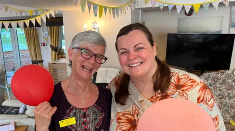 Susan Schibli and Krizsti Boros holding balloons in the lounge at Milward House