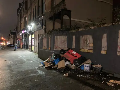 Flytipped rubbish next to wooden hoardings around a demolition site on Albert Drive, Pollokshields on 4 November 2024