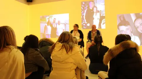 Northumbria Police A group of teenagers, shown from behind, listen to Connor Brown's dad, as photographs of the 18-year-old are projected on to a wall.