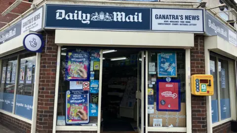 BBC/Dan Sambell The exterior of Ganatra's News in Coundon, Coventry. There is a yellow defibrillator box on the right of the picture, fixed to the exterior wall.