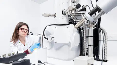 Historic England A female scientist in a white coat sitting at a white electro microscope