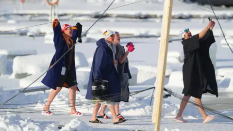 Erin Medcalf A group of ice swimming walking on a snowy plain in there swimming gear under dry robes.