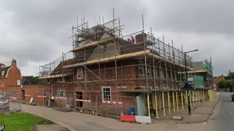A two-storey red brick building on a corner junction. It is covered in scaffolding. 