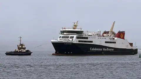 A large black and white ship with red funnels being guided by a tug