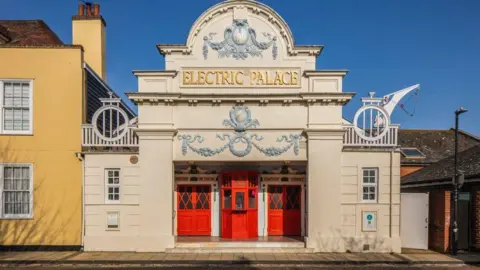 The outside of a building. It has a red door and Electric Palace written at the top