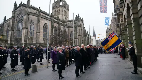 PA Media People stand in rows, many in military uniform, all facing Edinburgh's City Chambers, which has a UK and Scottish flag hanging from it. St Giles' Cathedral is behind them.