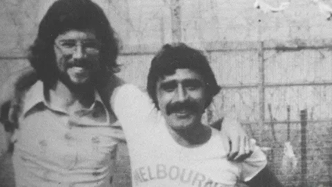 Pacemaker black and white photograph of two men with dark hair smiling broadly at the camera. The shorter of the two, Brendan Hughes, has his arm up and around the taller one's shoulder