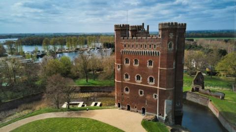 Tattershall Castle with four turrets surrounded by a moat, trees and a lake