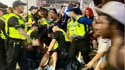 Your Southend At least seven police officers wearing hi-vis jackets detaining a person in Southend-on-Sea. The person is lying on their back on the floor.