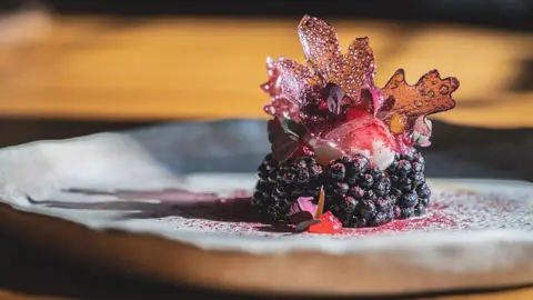 Moor Hall Blackberries, ragstone, verbena and apple marigold on a white plate on a wooden table