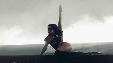 Henry Redcliffe Charli XCX on stage at Belsonic. She wears knee high boots, shorts and a black t shirt. There is smoke behind her.
