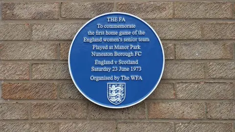 England Football A blue plaque reads: The FA, to commemorate the first home game of the England woman's senior team. Played at Manor Park, Nuneaton Borough FC, England v Scoaland, Saturday 23 ±June 1973, organised by The WFA"