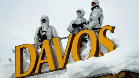 Getty Images Armed security personnel stand guard on the rooftop of a hotel, next to letters reading "Davos"