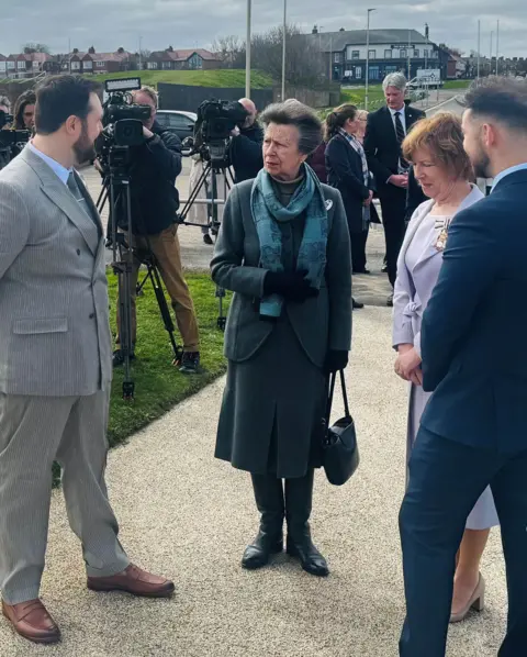 PA Media The Princess Royal arriving at the Colmans Seafood Temple in South Shields. She is wearing a smart blue-green suit. TV cameras are behind them.