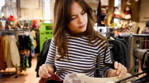 Getty Images A woman with long brown hair picks up items of clothing of the rack