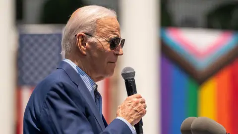 Getty Images Joe Biden holds a microphone while speaking in front of a Pride flag