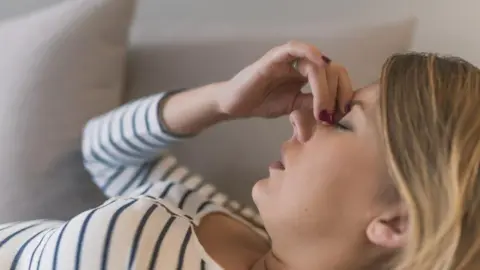 Close up of  blonde woman lying on a couch holding the bridge of her nose with 