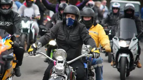 A convoy of motorbikes leaving the Woodhorn Museum in Ashington. They are all wearing leather jackets and helmets.