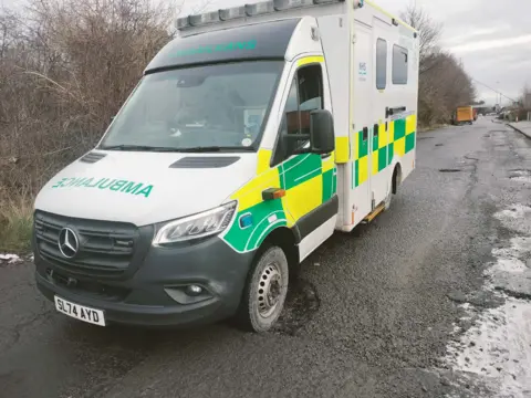 Alan Campbell An ambulance with its front passenger side wheel in a pothole