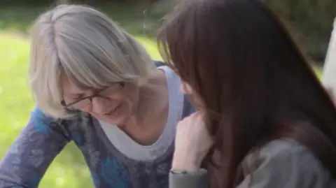 A woman reading something, with another woman with her back to the camera.