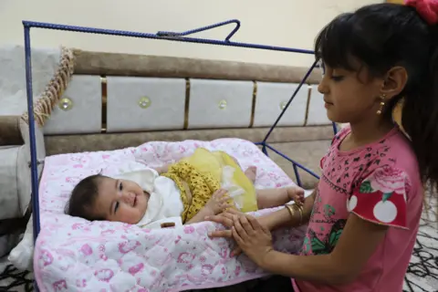 Baby Afraa on a swing being attended by her cousin