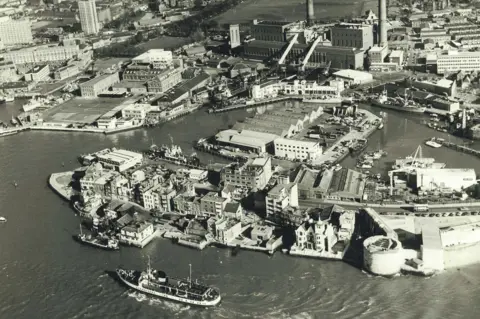 Portsmouth International Port	​​​​ An aerial black and white photo from the 70s. Long gone buildings line the coast.